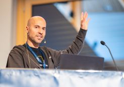 Alejandro Moreno López hält den Eröffnungsvortrag auf dem Drupal Mountain Camp 2025. Foto von Patrick Itten - patrickitten.ch / @patrickitten Sprecher steht am Rednerpult mit erhobener linketr Hand